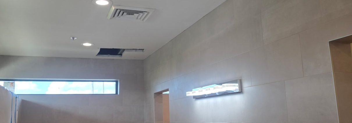 Commercial bathroom renovation with large-format tile, a double-sink vanity and new lighting by H3 Industries in Palm Beach Gardens
