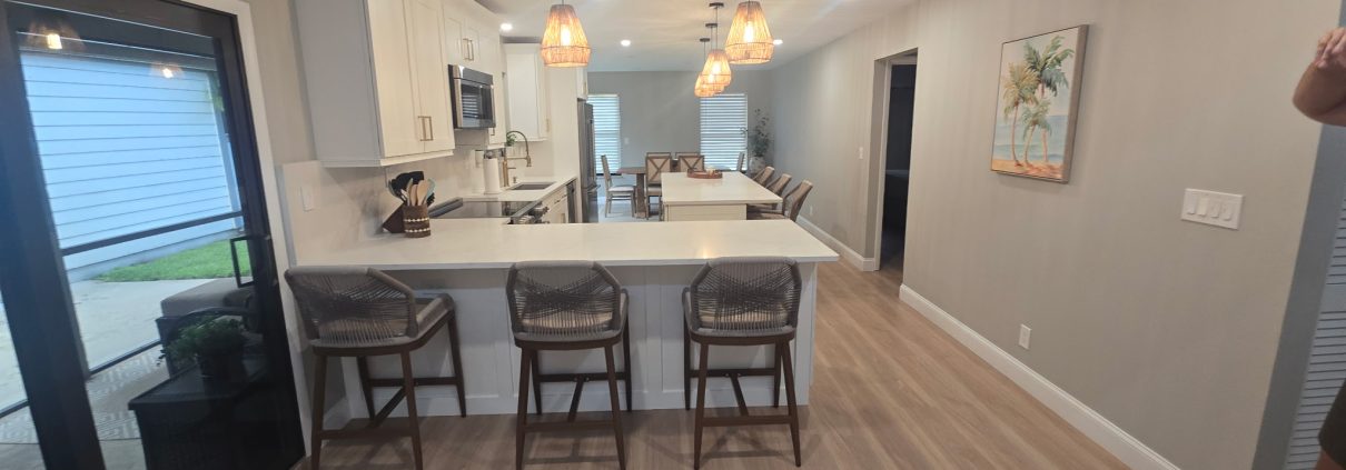 Open-plan kitchen remodel with island seating, pendant lights and wood-look flooring by H3 Industries in Palm Beach Gardens